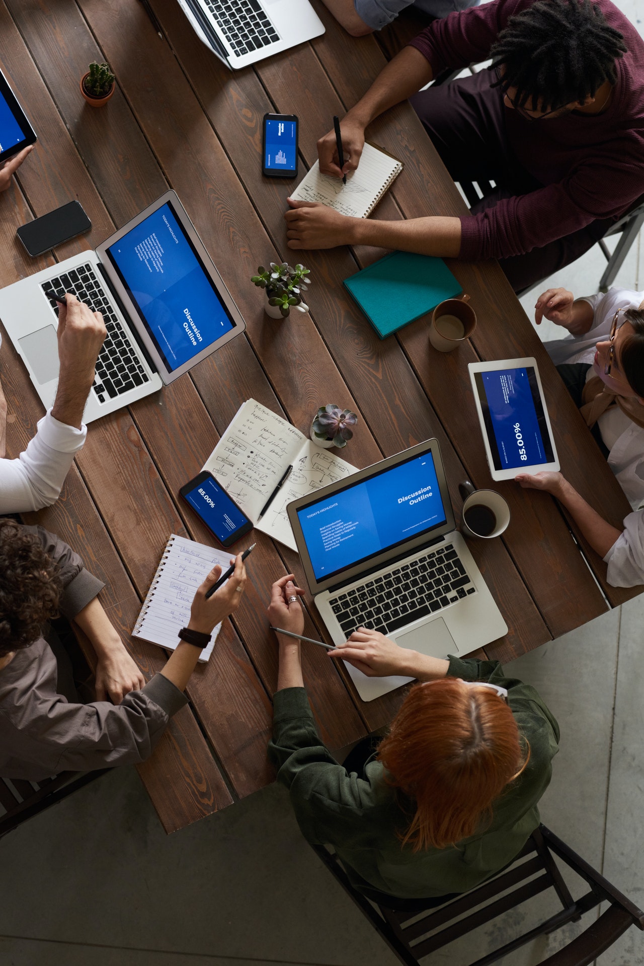 People Working on Devices At Wooden Table